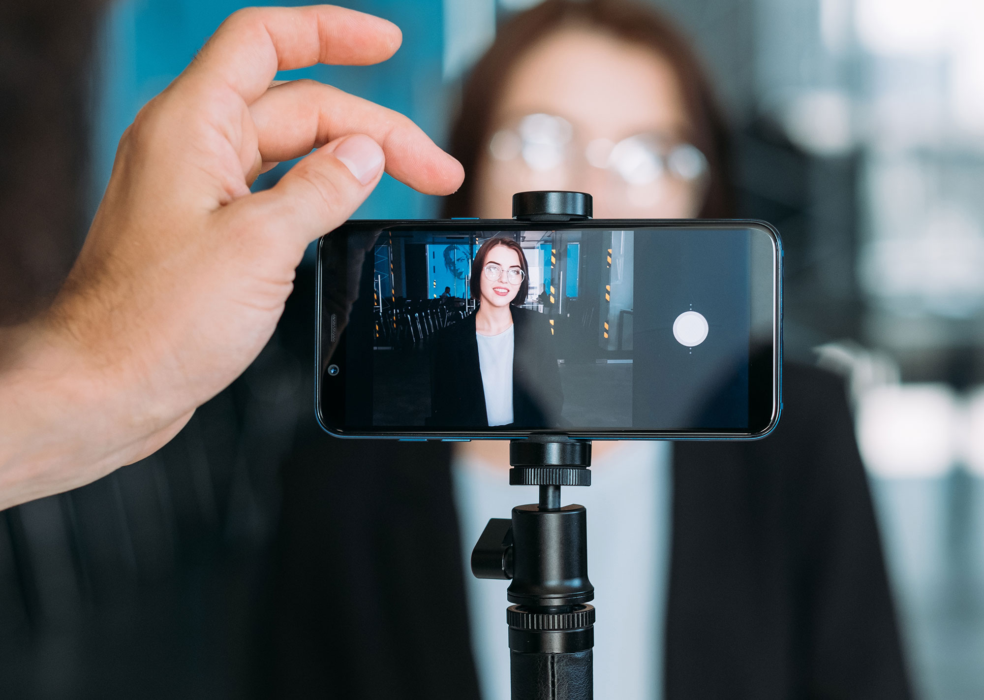 Man pressing record on phone while making presentation video with female coworker